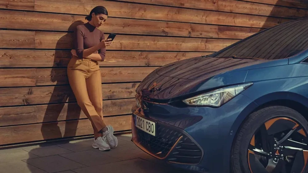 Vrouw kijkt naar haar mobiele telefoon terwijl ze naast een CUPRA Born staat
