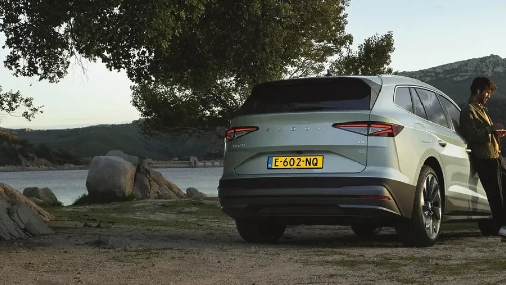 Man met laptop in de hand leunend tegen een Škoda Enyaq