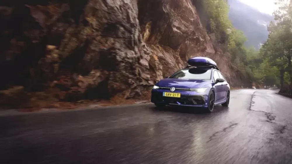 Blauwe Volkswagen Golf met dakkoffer op een natte weg