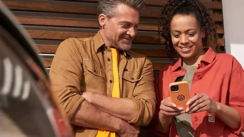 Vrouw en man kijken naar een telefoon in de hand van de vrouw, leunend tegen een garage
